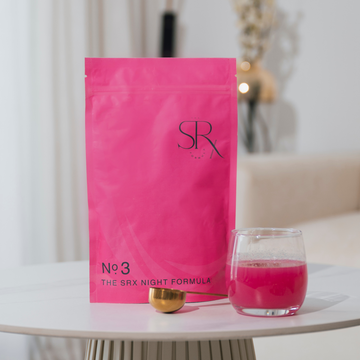 A sealed pink pouch labelled 'SRX' with the text 'No.3 THE SRX NIGHT FORMULA' is displayed next to a pink glass of water and a golden object, presented on a white surface with a blurred background.
